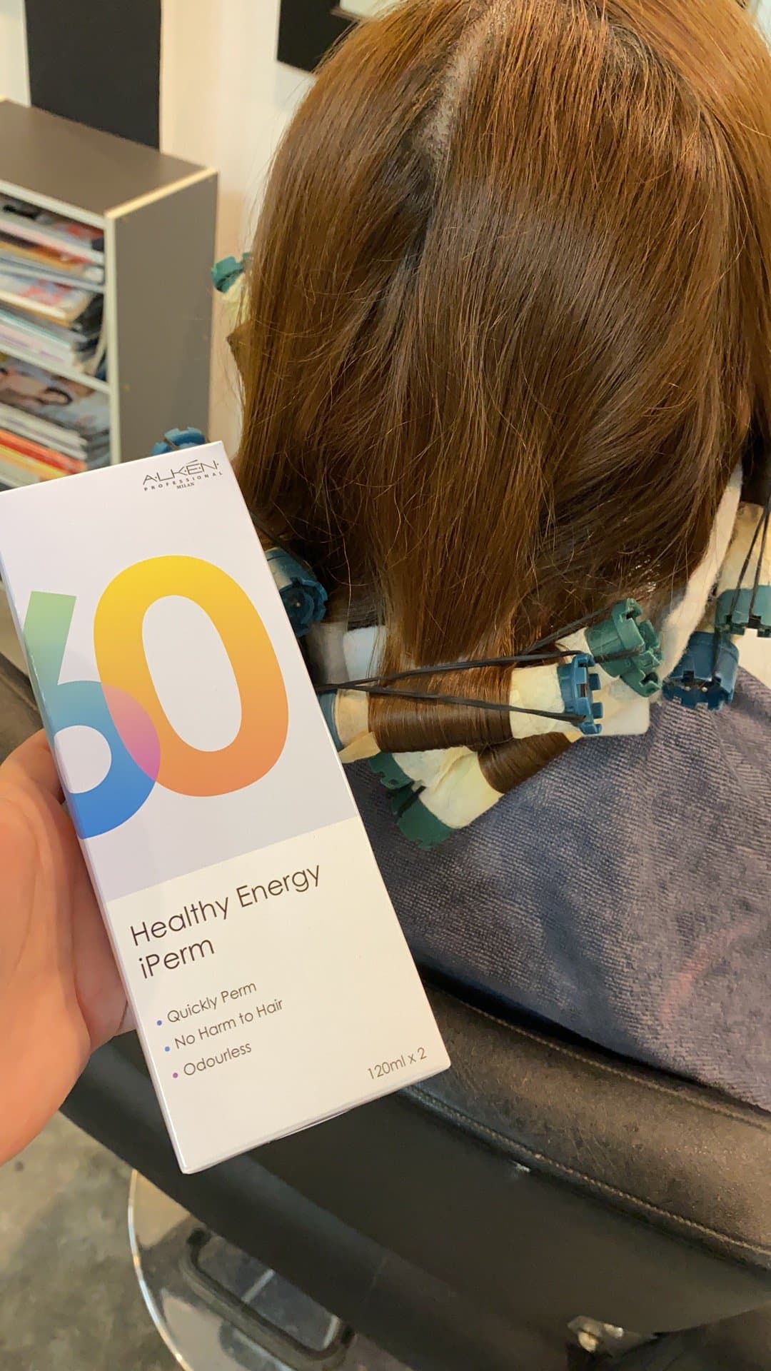 A stylist holds the iPerm box beside a client whose hair is wound on perm rods