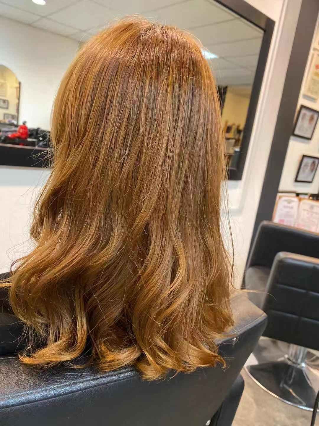 The back of a client's shoulder-length copper hair with loose waves, in a salon chair